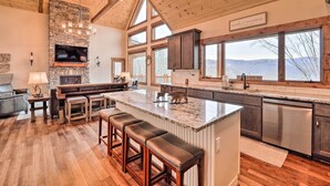 A spacious kitchen with a large island, stone fireplace, and large windows offering a view of the outdoors. - Mountainside Family Retreat w/ Deck in Banner Elk! (Banner Elk)