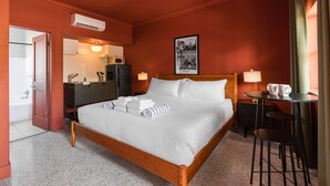 A hotel room with a wooden bed, a small kitchenette, a bathroom, and a dining area with a table and chairs.