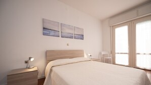 Une chambre à coucher comprenant un lit, une table de chevet, une lampe, une chaise et une œuvre d’art accrochée au mur.