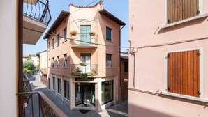 Un immeuble avec un commerce au rez-de-chaussée, un balcon orné de plantes et un volet en bois sur le côté droit.