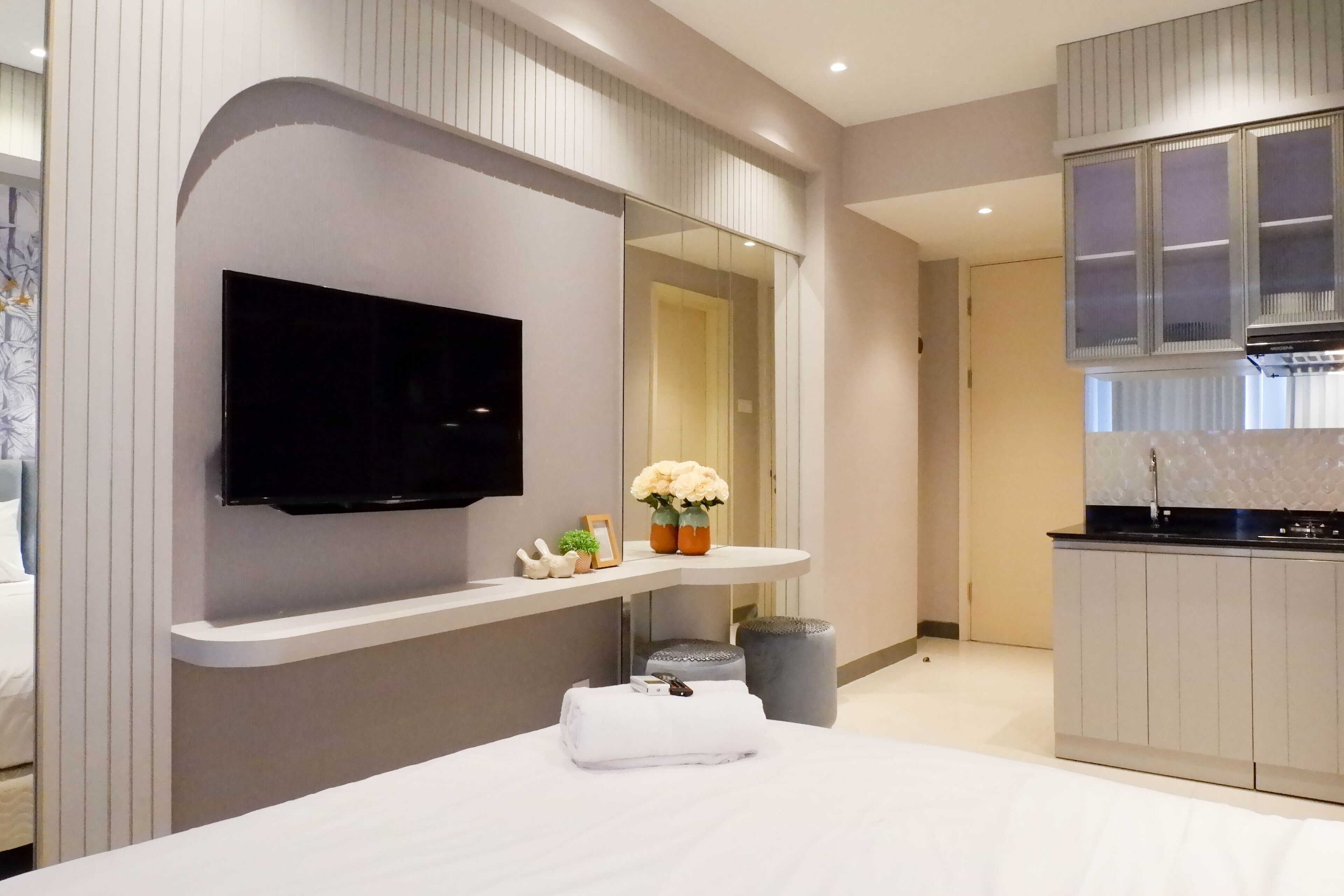 Een moderne hotelkamer met een groot bed, een flatscreen televisie aan de muur, een klein kaptafel met spiegel, een keukenhoek met kasten en een prullenbak.