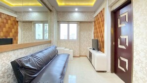 A modern living room with a leather sofa, a TV on a white stand, and a patterned wall. - Modern 2Br Apartment At Suites @Metro (Bandung)