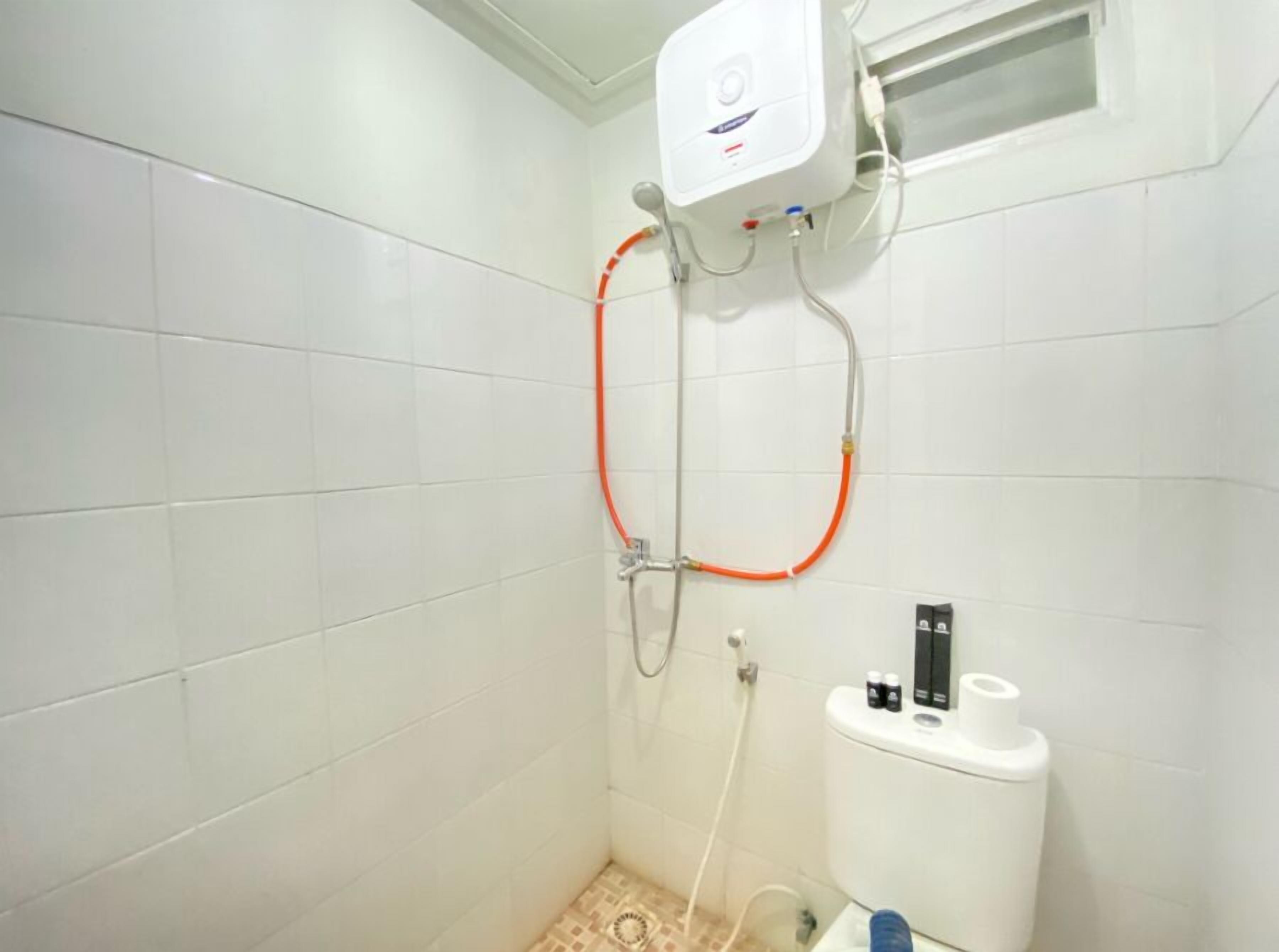 A small, tiled bathroom with a shower, a toilet, and a water heater mounted on the wall.