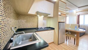 Een kleine keuken met een spoelbak, fornuis en koelkast. Er is een eethoek met een tafel en stoelen.