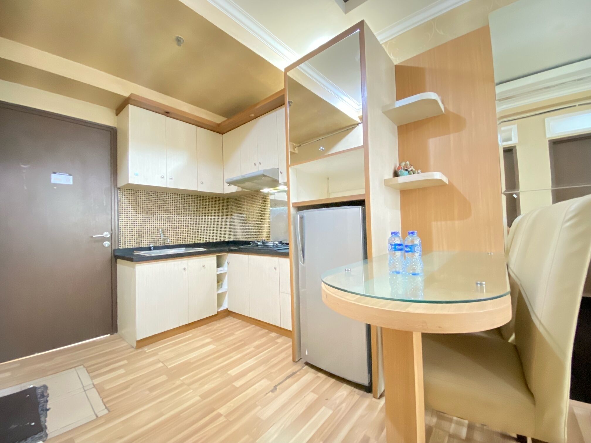 A compact kitchen with a refrigerator, a sink, and a glass table.