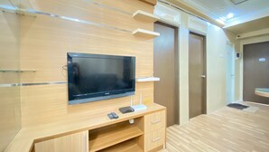 Een moderne woonkamer met een flatscreen televisie bevestigd aan een houten wand, een klein houten kastje eronder en een deur aan de rechterkant.