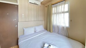 Een hotelkamer met een bed, een airconditioning, een raam met gordijnen en een deur.