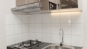 A modern kitchen with a gas stove, stainless steel sink, and white tiled walls. - Cozy Stay 2Br Springlake Summarecon Bekasi Apartment (Bekasi)