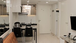 A modern kitchen with white cabinets, a dining area with a brown couch, and a TV mounted on the wall. - Cozy Stay 2Br Springlake Summarecon Bekasi Apartment (Bekasi)
