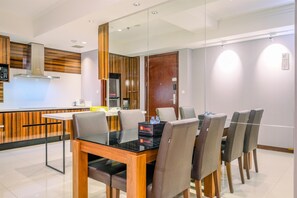 A modern dining area with a glass-top table, six chairs, and a kitchen in the background.