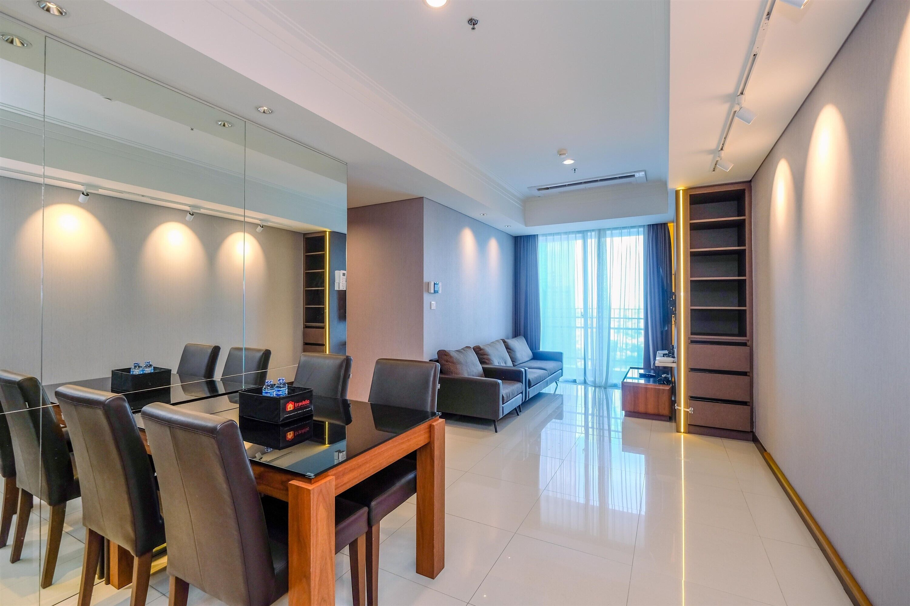 A modern hotel room with a dining area, a sofa, and a built-in bookshelf.