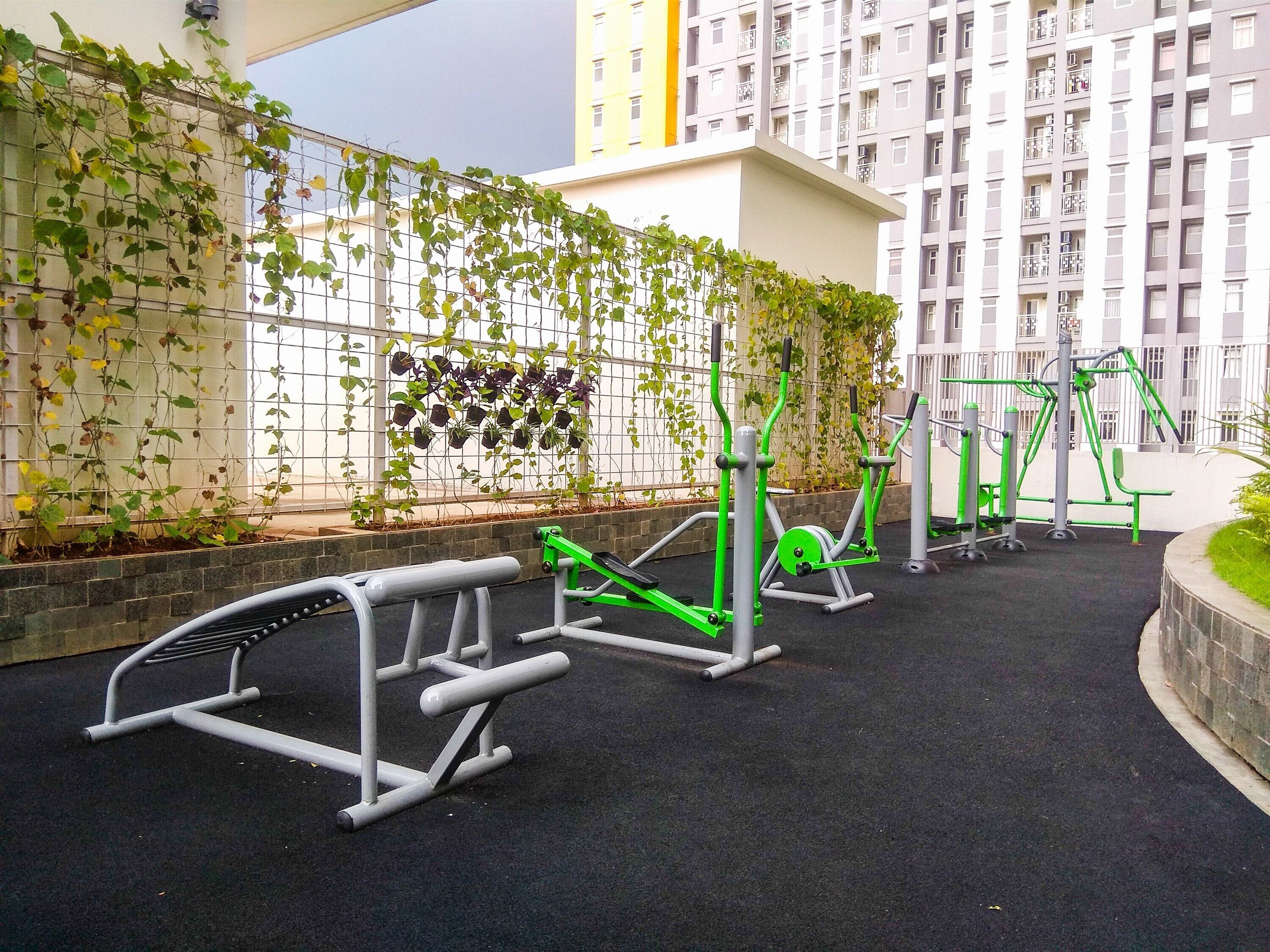Zona de gimnasio al aire libre con equipo de ejercicio, pared de escalada y un edificio al fondo.