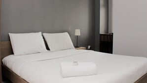 A neatly made bed with white linens and pillows, a bedside lamp, and a wooden nightstand.