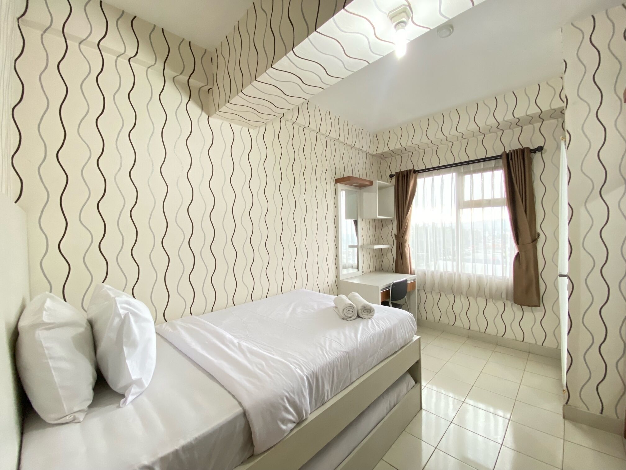 A hotel room with a bed, a desk, a mirror, and a window with curtains.