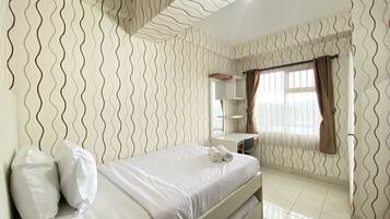 A hotel room with a bed, a desk, a mirror, and a window with curtains.