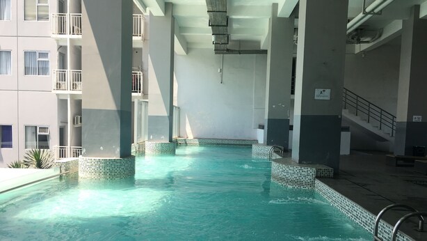 An indoor swimming pool with tiled edges and a clear blue water surface, surrounded by a building with balconies and a staircase.