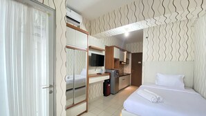 A hotel room with a bed, a desk, a TV, and a kitchenette.