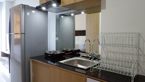 A modern kitchen with a stainless steel refrigerator, a black countertop, a sink, and a wire rack.