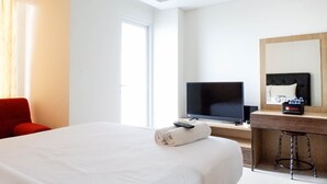 A hotel room with a large bed, a TV, a desk with a mirror, and a red chair.