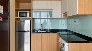 A compact kitchen with a stainless steel refrigerator, a microwave, and a washing machine.