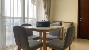 A dining area with a table and four grey chairs, a black box labeled 'Travelio', and a view of the city through large windows.