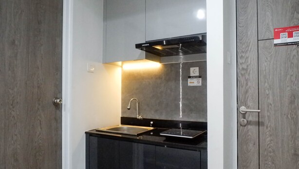 Una cocina compacta con un lavamanos de acero inoxidable, una encimera negra y una campana extractora moderna.