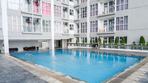 Una piscina con escalera metálica, rodeada por un edificio con varios balcones y ventanas.