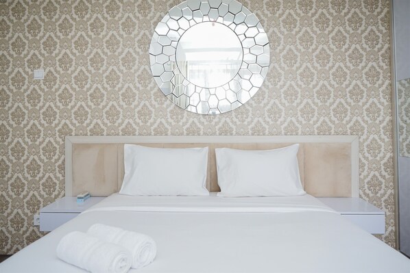 Ein Hotelzimmer mit einem Bett, zwei weißen Kissen, einem runden Spiegel an der Wand und einem Wandpapier mit Muster.