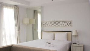 Een hotelkamer met een groot bed, een nachtkastje met een lamp, een ander nachtkastje met een klok, en een spiegel aan de muur.