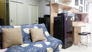 A compact living space with a sofa, a refrigerator, a microwave, and a small kitchen area with stools. - Comfy And Modern Wonderful 2Br Apartment At Tanglin Supermall Mansion (Surabaya)