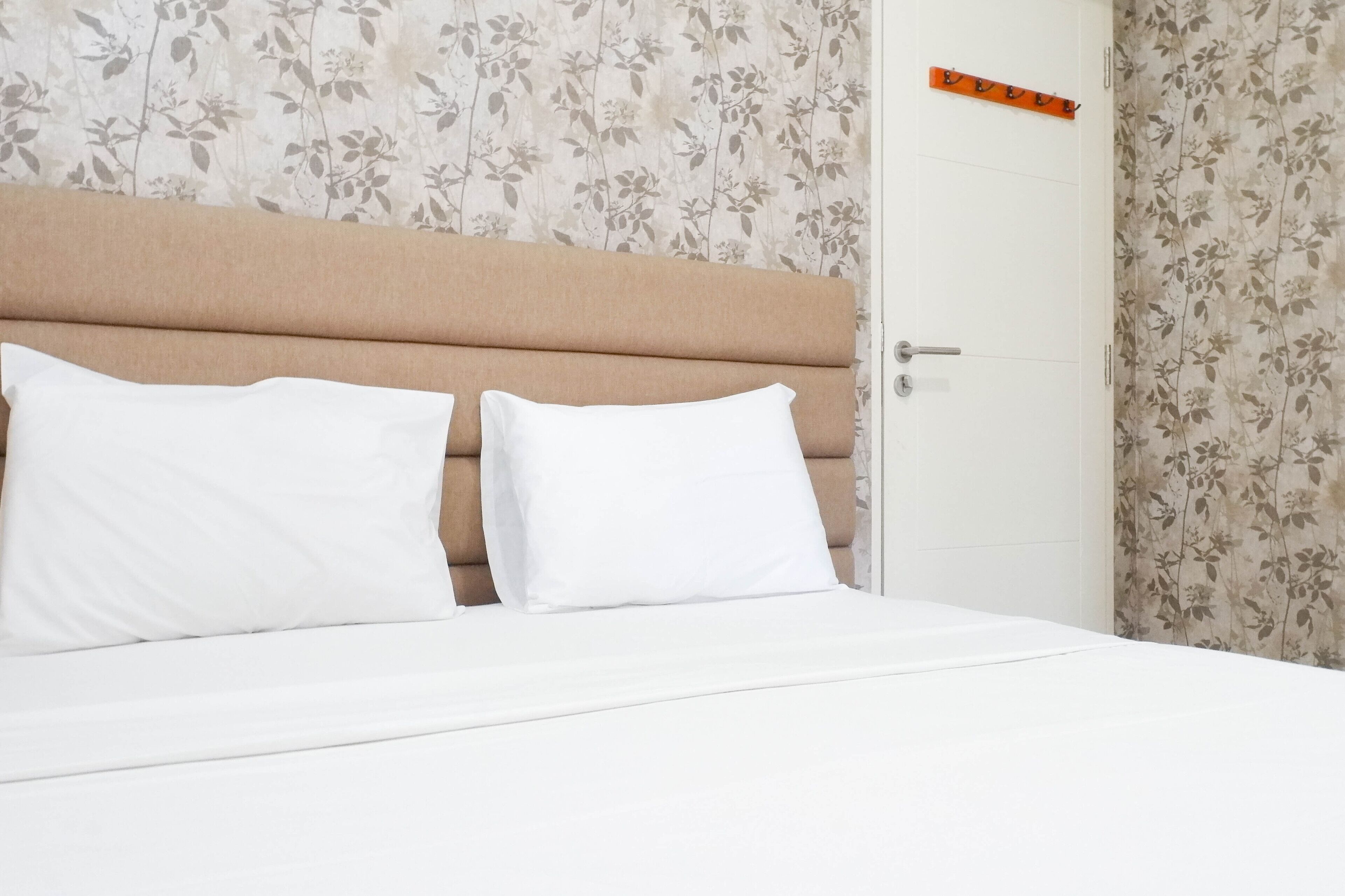 A neatly made bed with two pillows, a wooden headboard, and floral wallpaper.