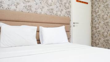 A neatly made bed with two pillows, a wooden headboard, and floral wallpaper.