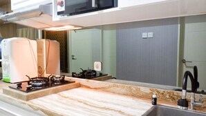 A kitchen with a marble countertop, a sink, a stove, and a water heater. - Comfy And Modern Wonderful 2Br Apartment At Tanglin Supermall Mansion (Surabaya)