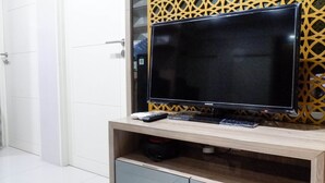 A flat-screen TV on a wooden stand with a remote control and a smartphone. - Comfy And Modern Wonderful 2Br Apartment At Tanglin Supermall Mansion (Surabaya)