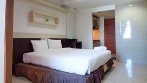 A modern hotel room with a large bed, a bedside table, a small shelf, and a door leading to another room. - Best Deal Studio Apartment At High Point Serviced (Surabaya)