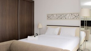 A hotel room with a bed, a sofa, a lamp, and a wall art piece. - Warm And Cozy Studio At Azalea Suites Apartment (Cikarang)