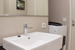 A bathroom with a white sink, a mirror, and a wall-mounted heater. - Warm And Cozy Studio At Azalea Suites Apartment (Cikarang)