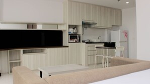 A compact living space with a kitchenette, a sofa, a dining table, and a TV. - Warm And Cozy Studio At Azalea Suites Apartment (Cikarang)