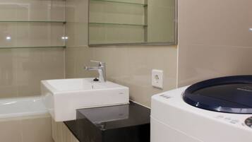 A modern bathroom with a white sink, a black countertop, and a built-in washing machine.