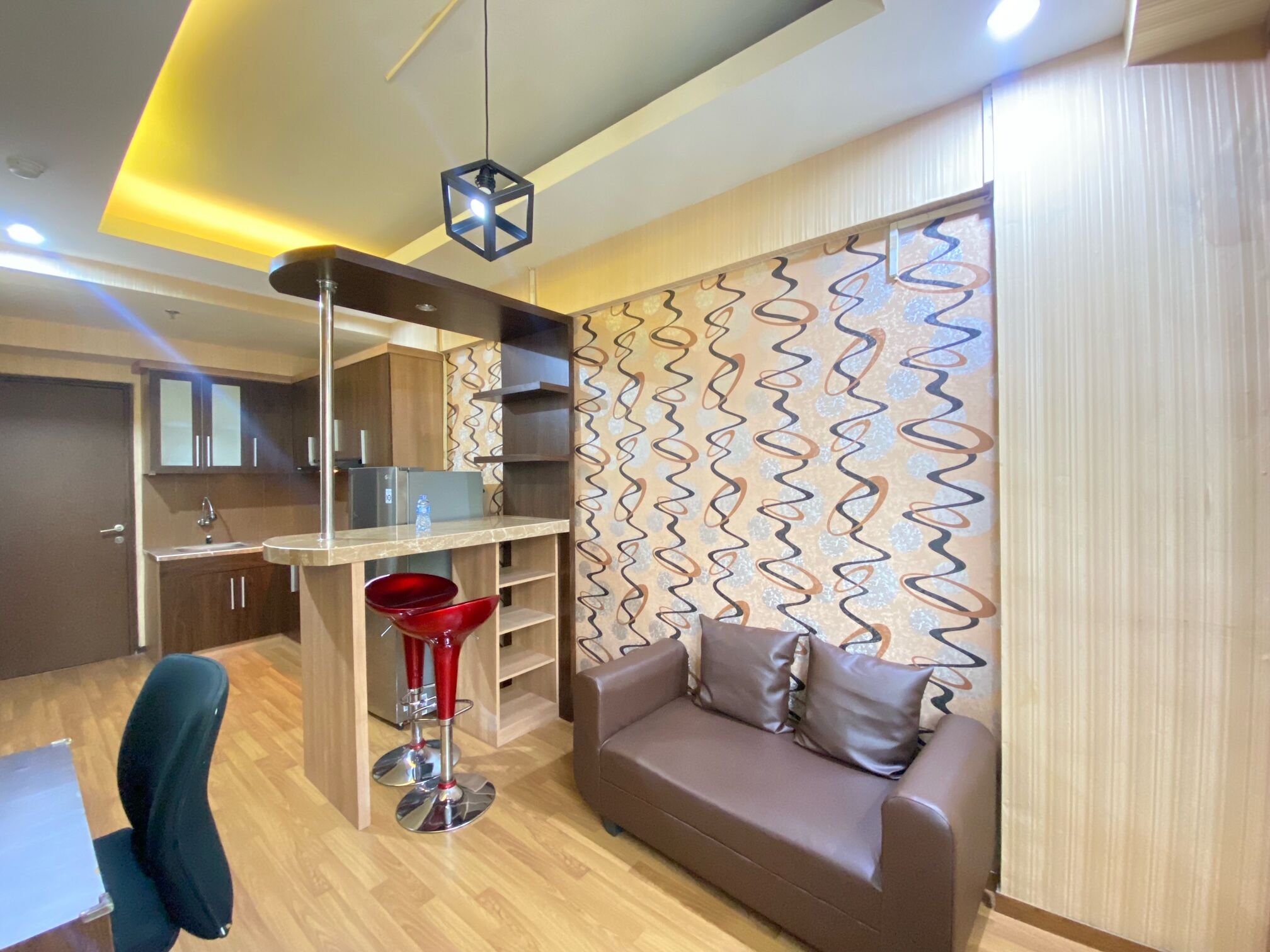 A modern kitchen with a central island, a dining area with a red chair, and a brown sofa with cushions.