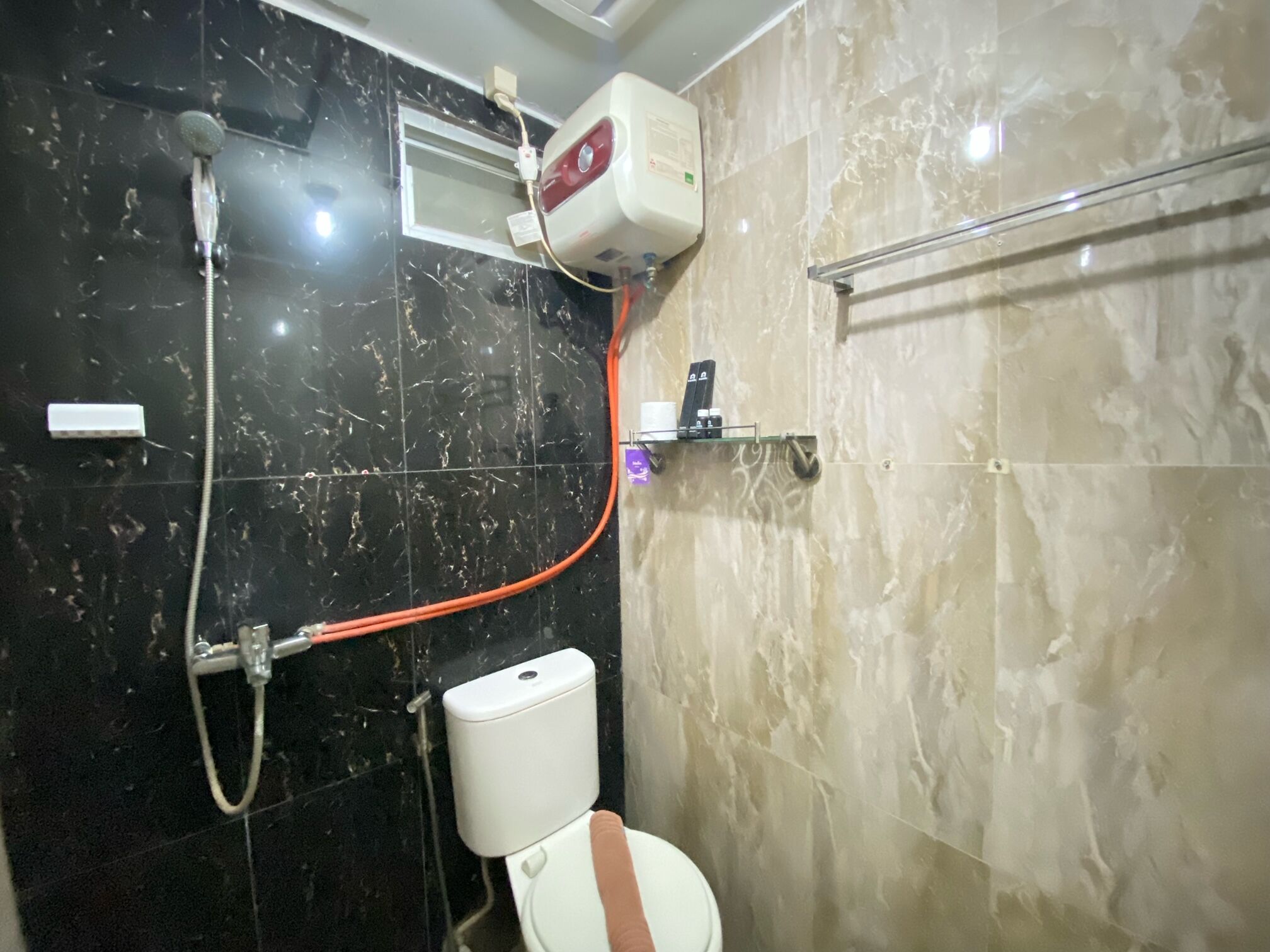 Une salle de bain avec un mur en marbre noir, un mur en marbre beige, une pomme de douche, des toilettes et un porte-serviettes.