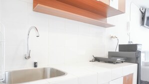 Een moderne keuken met een RVS spoelbak, witte tegels, houten keukenkastjes en een ingebouwde magnetron.
