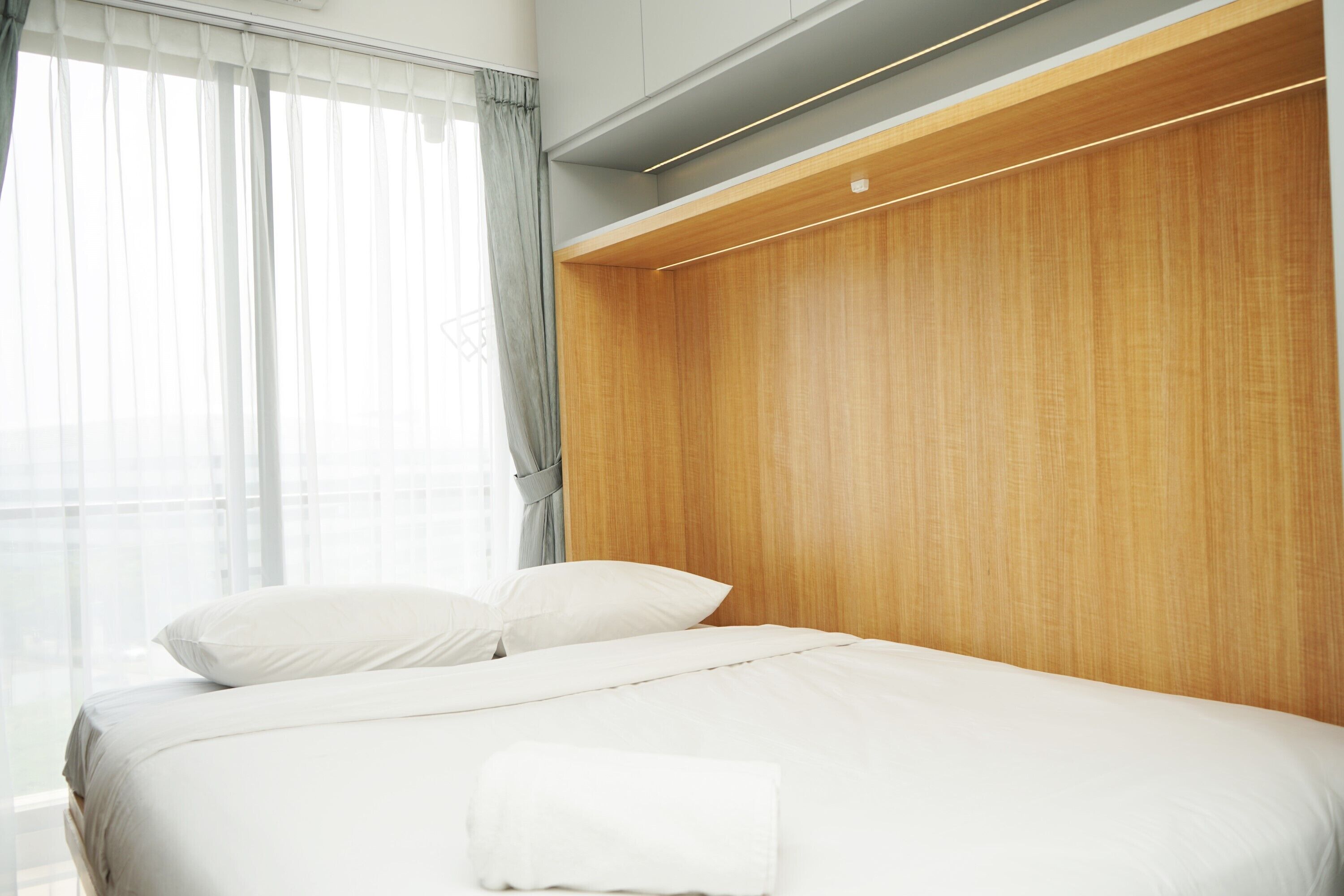 Une chambre d’hôtel moderne avec un lit, une tête de lit en bois et une grande fenêtre avec des rideaux.