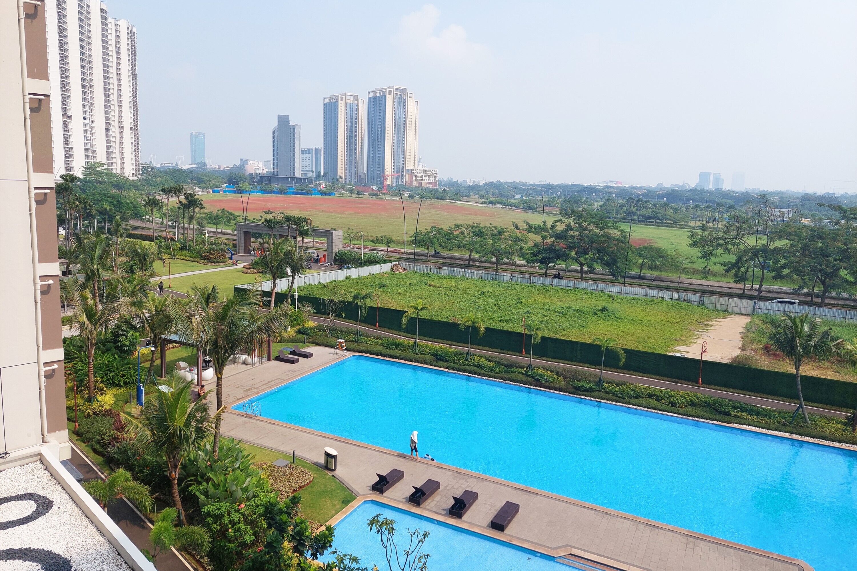 A swimming pool with lounge chairs, surrounded by greenery and a sports field.