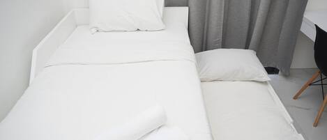 A single bed with white bedding and pillows, a grey curtain, and a black chair with wooden legs.