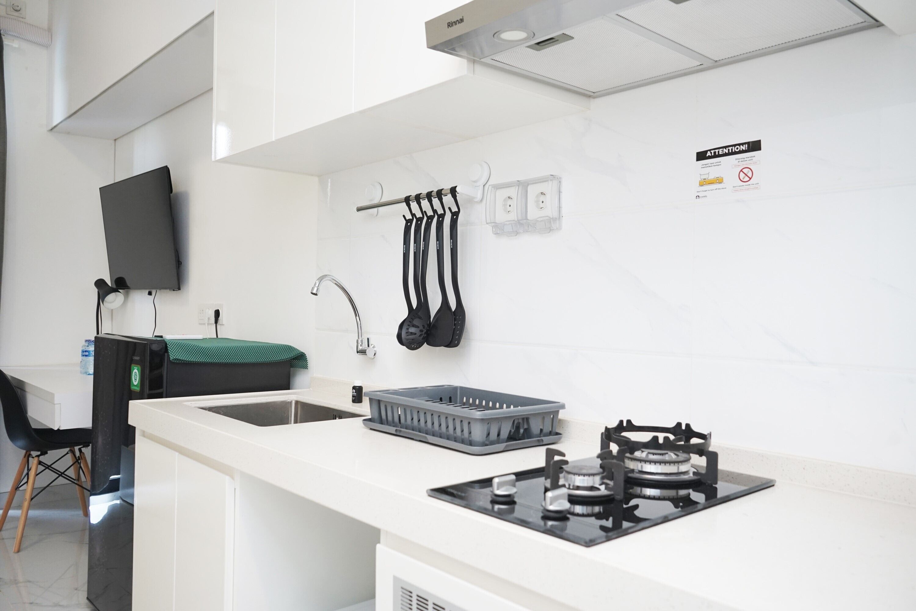 A modern kitchen with a white countertop, a gas stove, a sink, and a black chair.