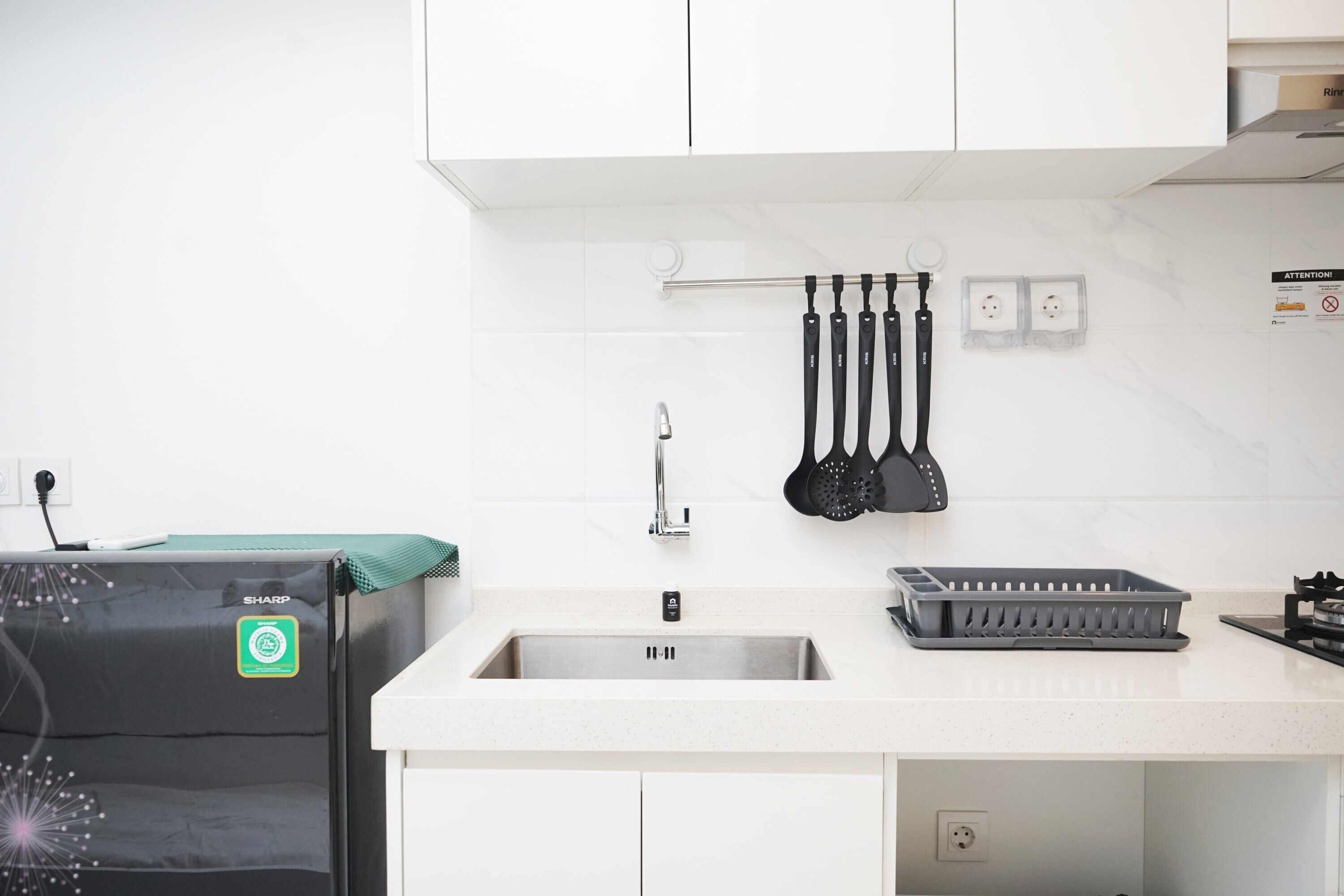 A modern kitchen with white cabinets, a stainless steel sink, and a black Sharp refrigerator.