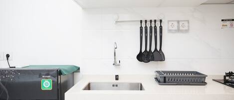 A modern kitchen with white cabinets, a stainless steel sink, and a black Sharp refrigerator.