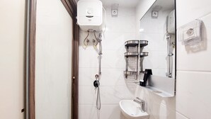 Une salle de bain moderne avec un lavabo blanc, un miroir, une douche équipée d’un pommeau de douche à main et un distributeur de serviettes.