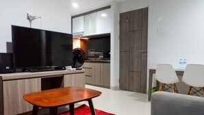 A modern kitchen with a flat-screen TV, a dining area with two chairs, and a red rug. - Best Price 2Br With Pool View Apartment At Taman Melati Surabaya (Surabaya)